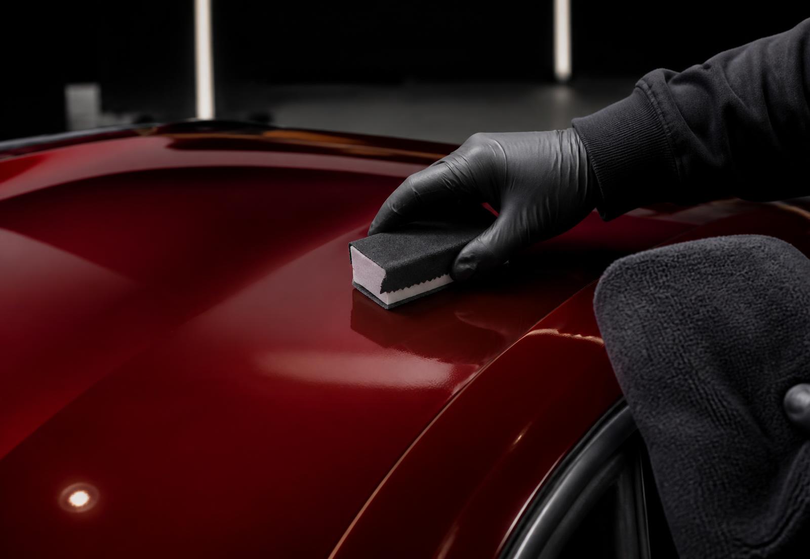 Gloved hand applying paint protection to the roof of a deep red sports car