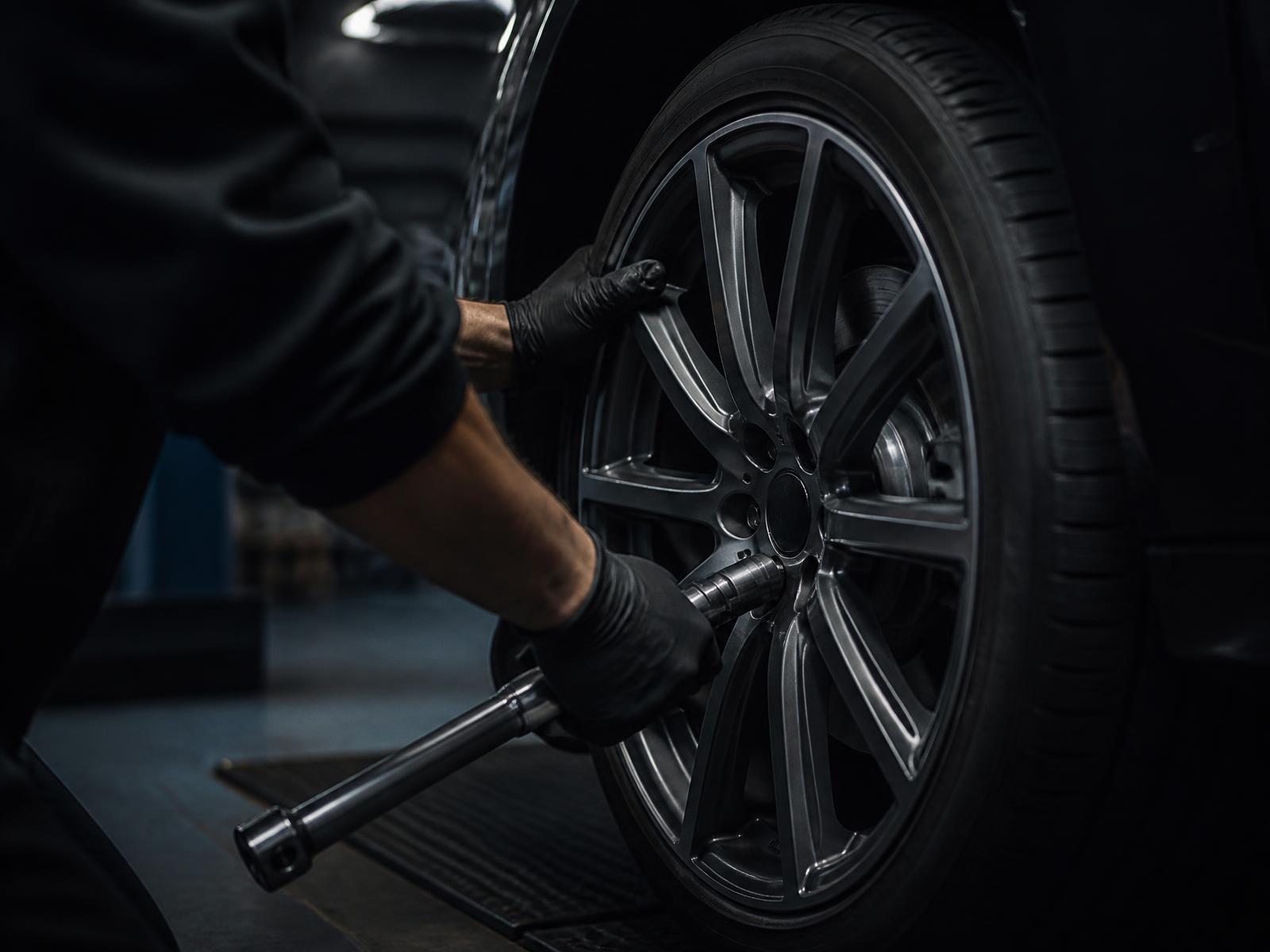 Technician fitting an alloy wheel and torquing the fasteners on a dark vehicle